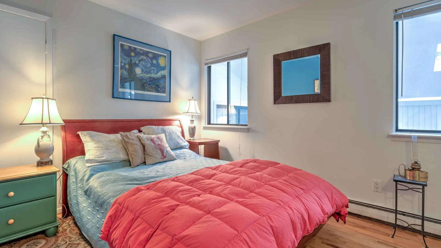 A bedroom with a bed dressed in a red quilt and blue bedding.