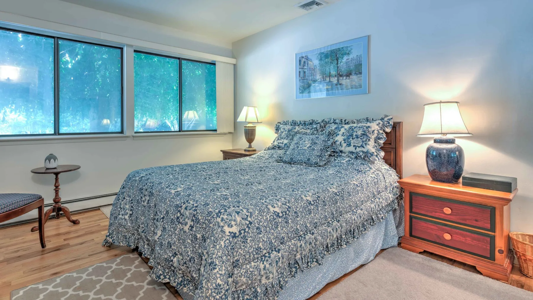 A bedroom with a bed covered in patterned bedding and large windows.