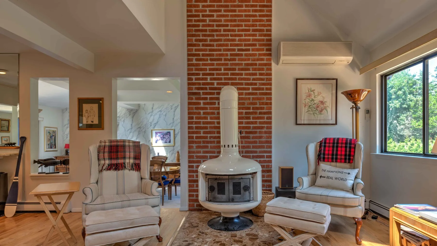 A bright living room with a central fireplace and seating beside large windows.