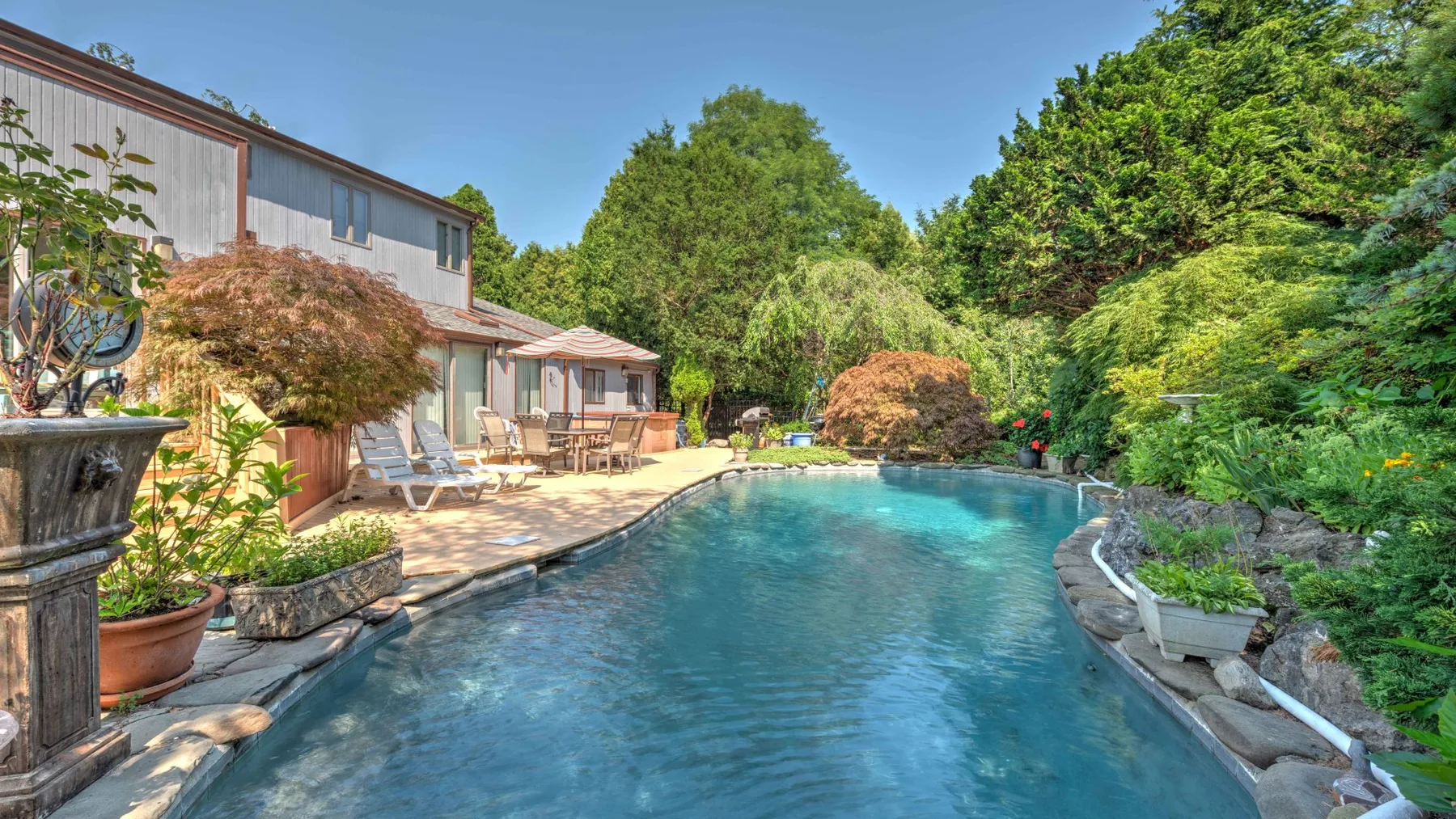 An outdoor swimming pool beside a house, with lounge seating along the deck.