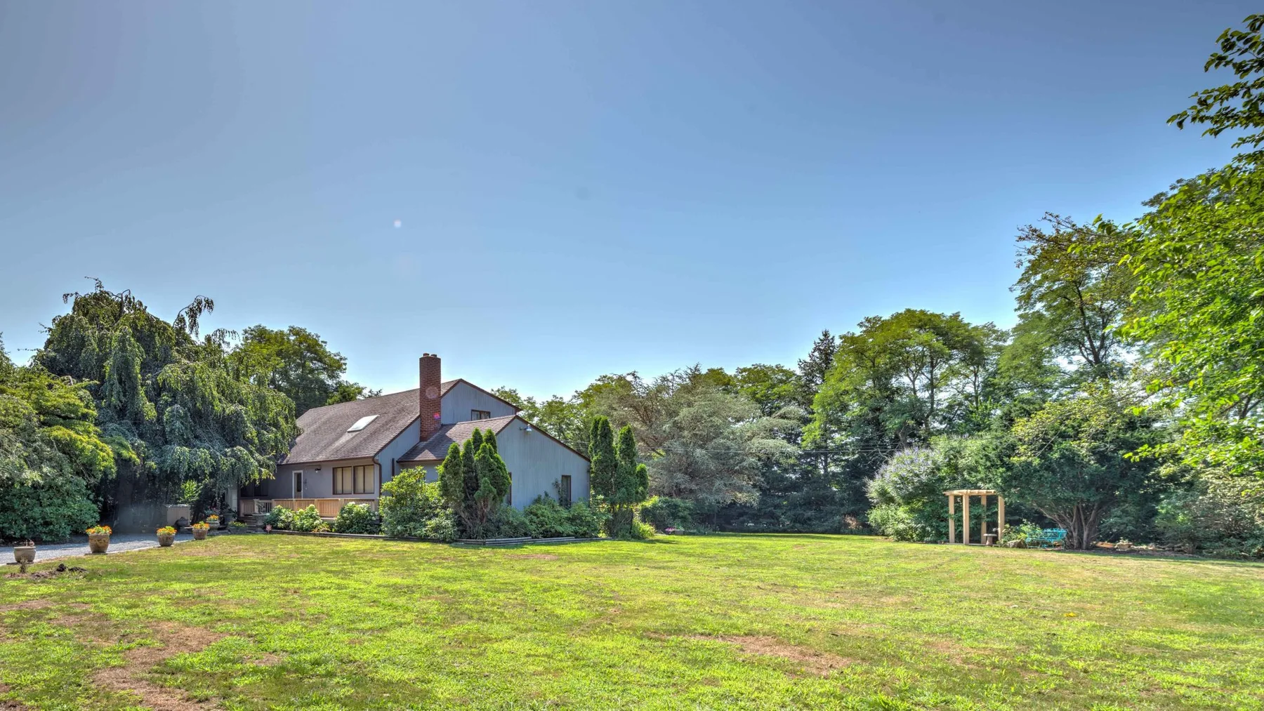 A house stands beyond a broad grassy lawn, surrounded by trees.
