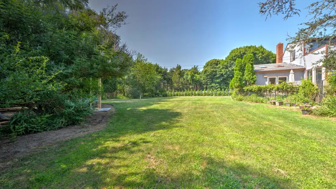 A grassy garden bordered by trees, with a house visible at the edge.