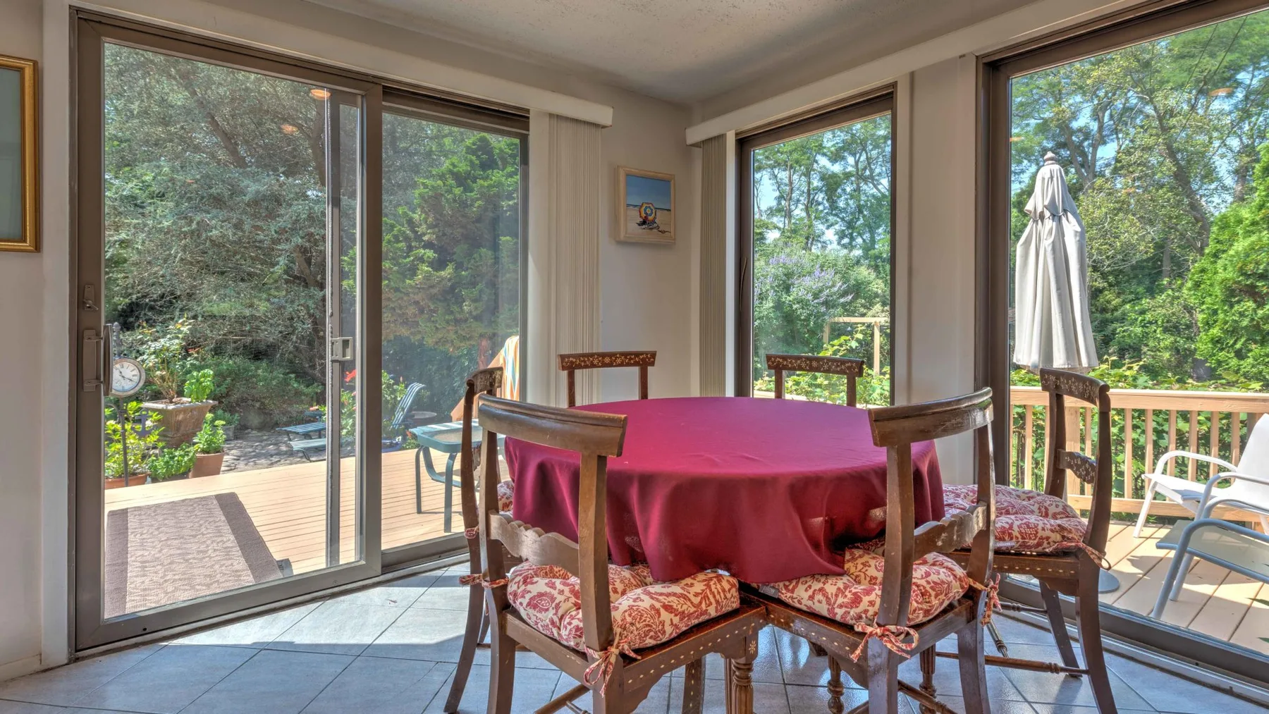 A dining area with a round table and chairs beside large windows overlooking greenery.