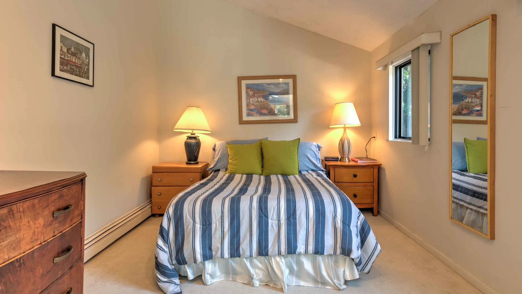 A bedroom with a striped bedspread, green pillows, and matching bedside lamps.