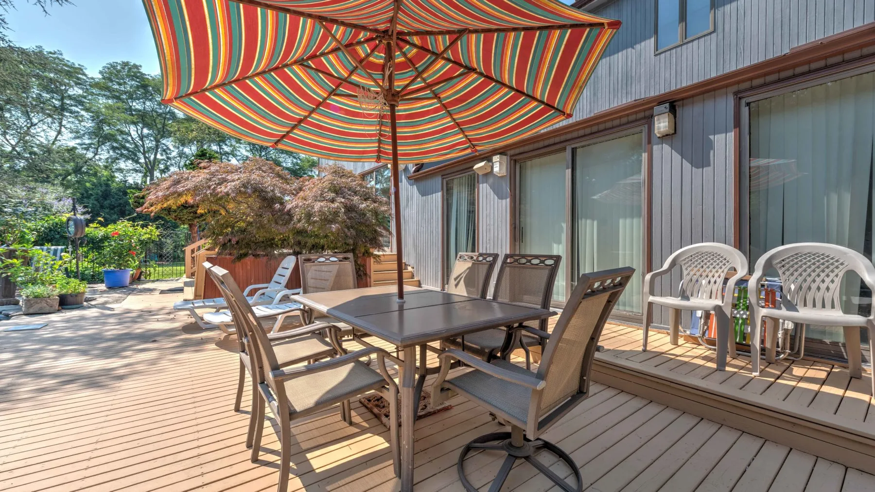 An outdoor deck dining area sits beneath a striped umbrella beside the house.