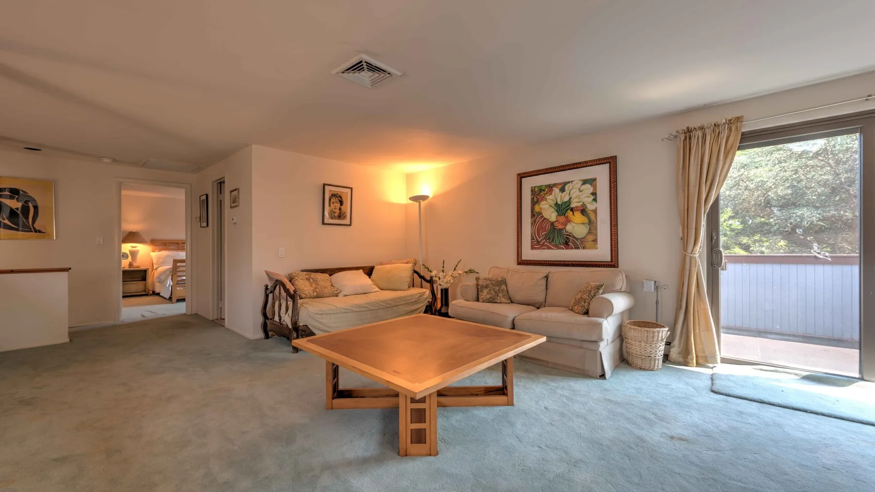 A living room with seating, a coffee table, and a sliding glass door to a balcony.
