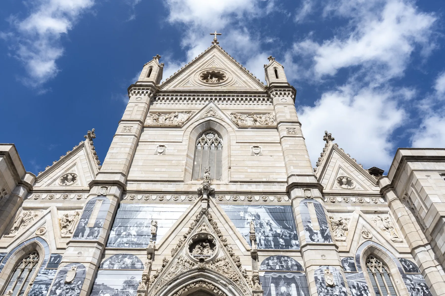 La ornamentada fachada de piedra de una iglesia gótica se alza contra un cielo azul con nubes.