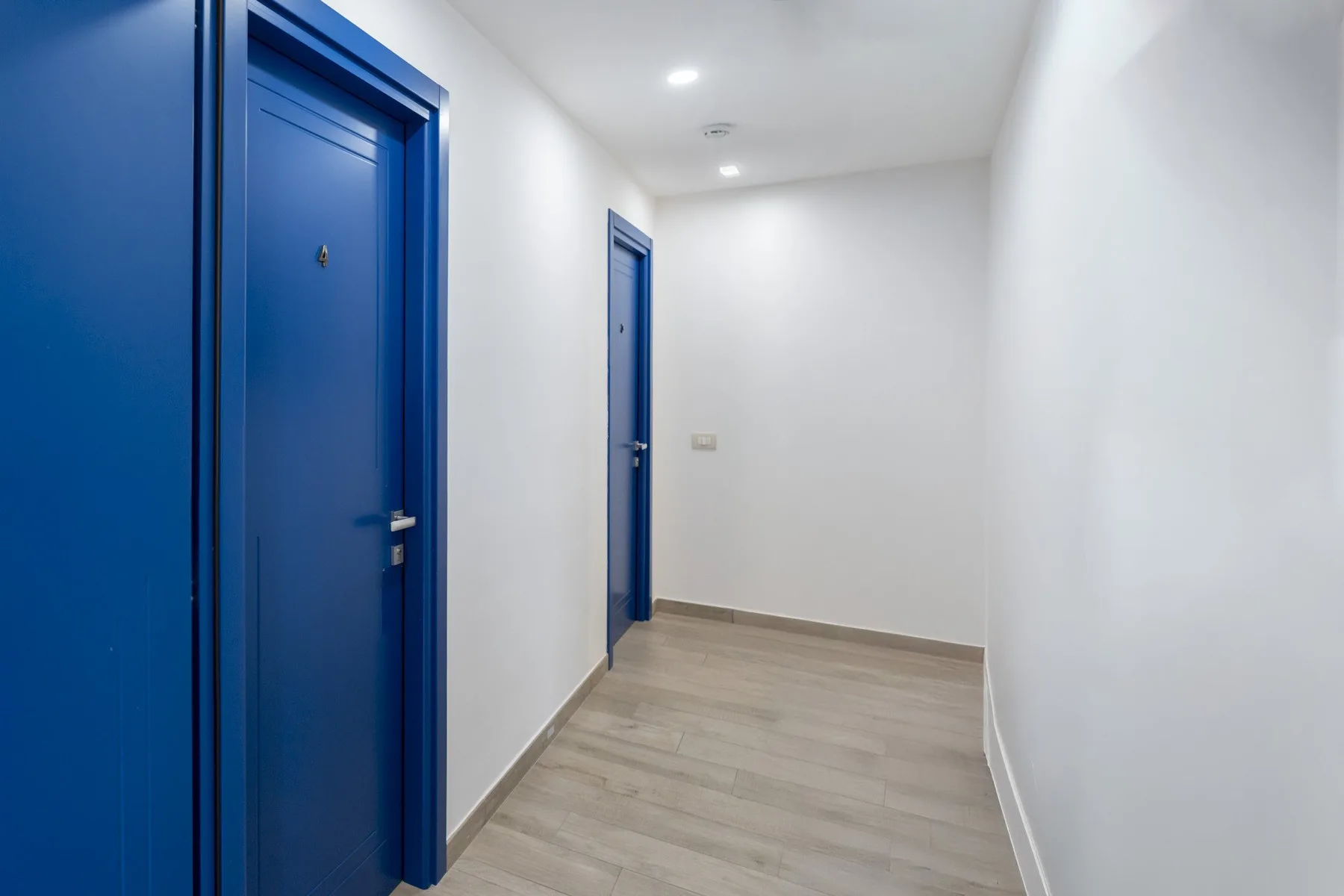 Un pasillo luminoso con puertas azules y suelo de tono claro.