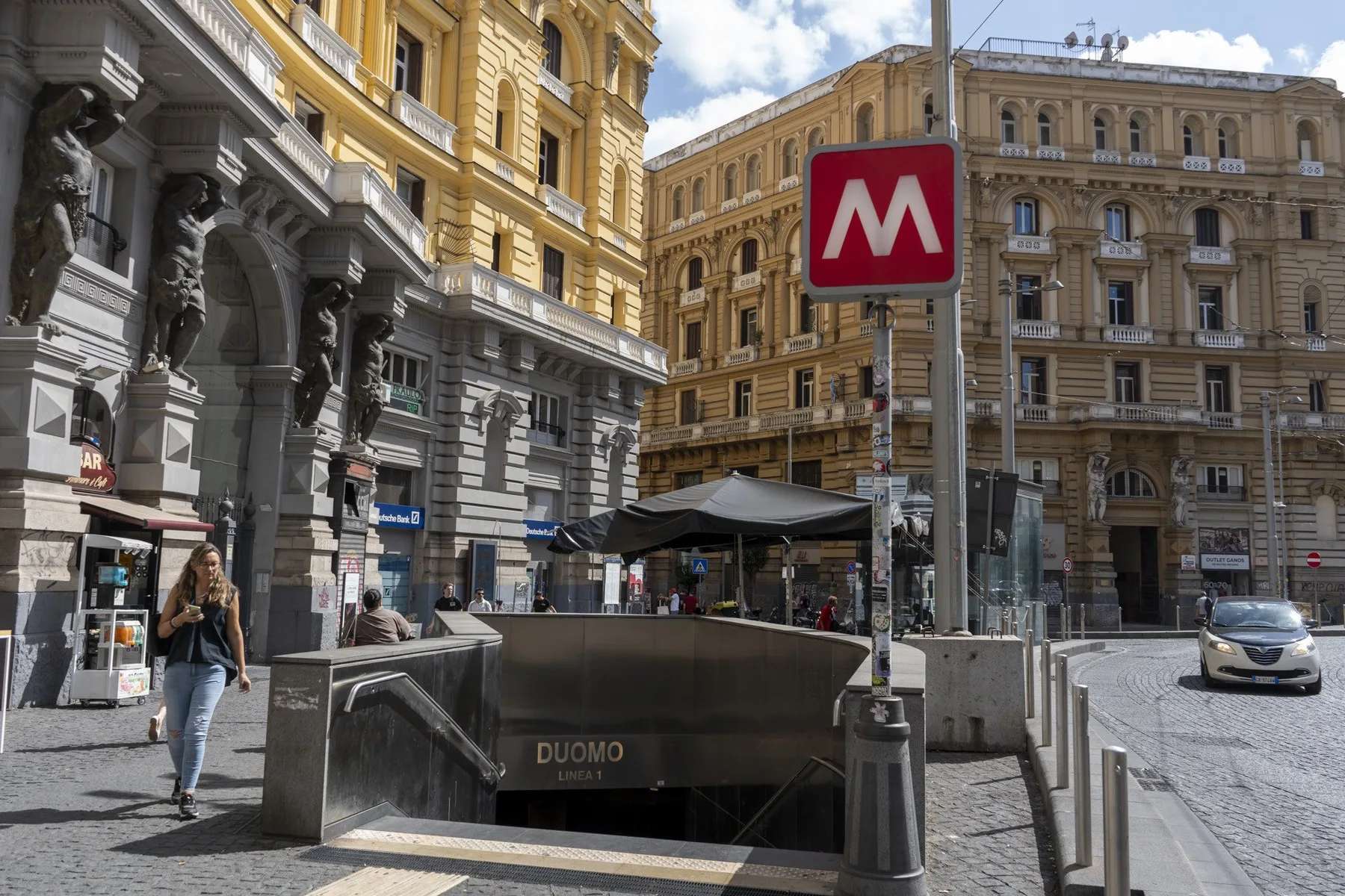 Una calle urbana con edificios de piedra ornamentados y una entrada al metro.
