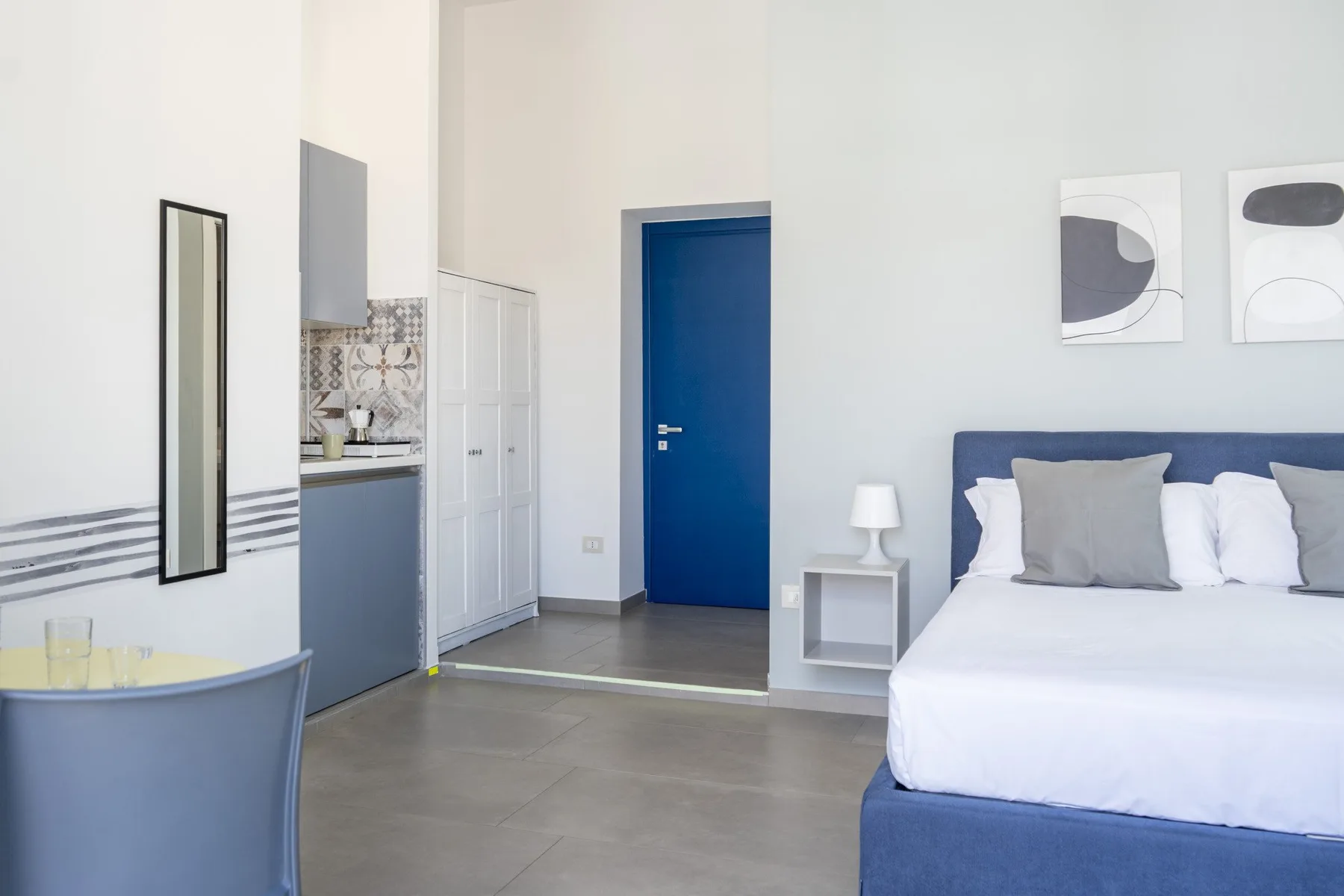 Un dormitorio luminoso con cama, mesita de noche y cocina pequeña.