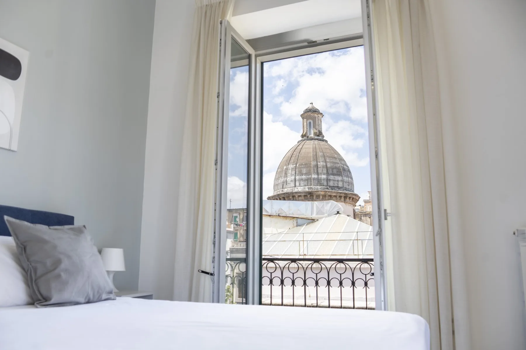 Un dormitorio con una cama junto a una ventana abierta con vistas a un edificio con cúpula.