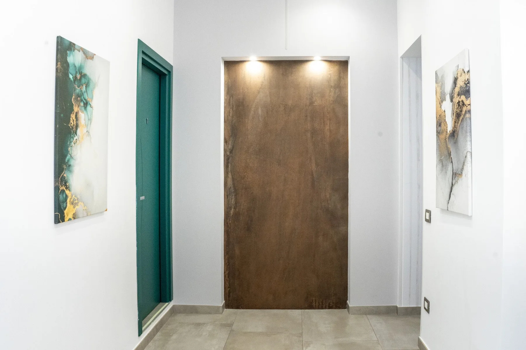 Un pasillo luminoso con una puerta de madera oscura y arte abstracto en las paredes.