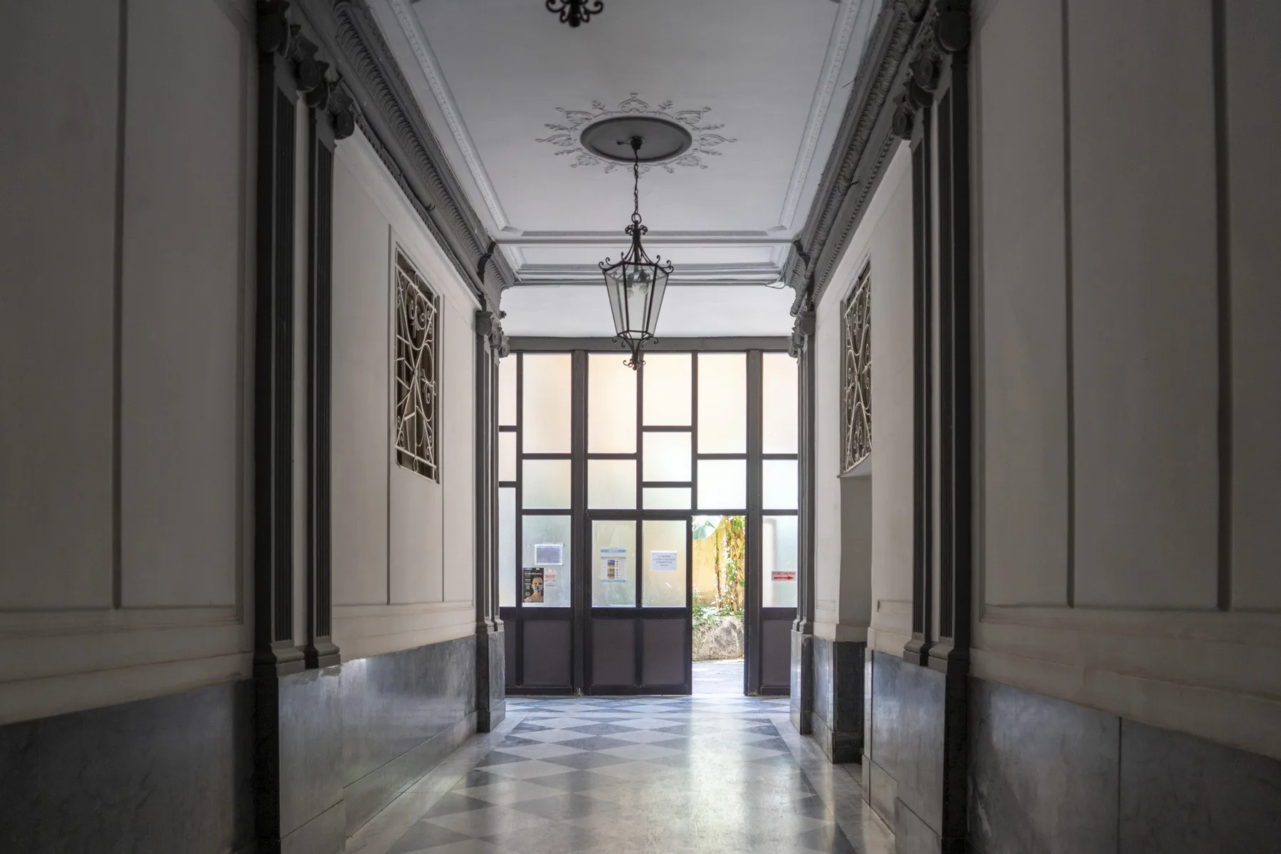 Un pasillo interior luminoso con paneles decorativos en las paredes y una entrada acristalada.