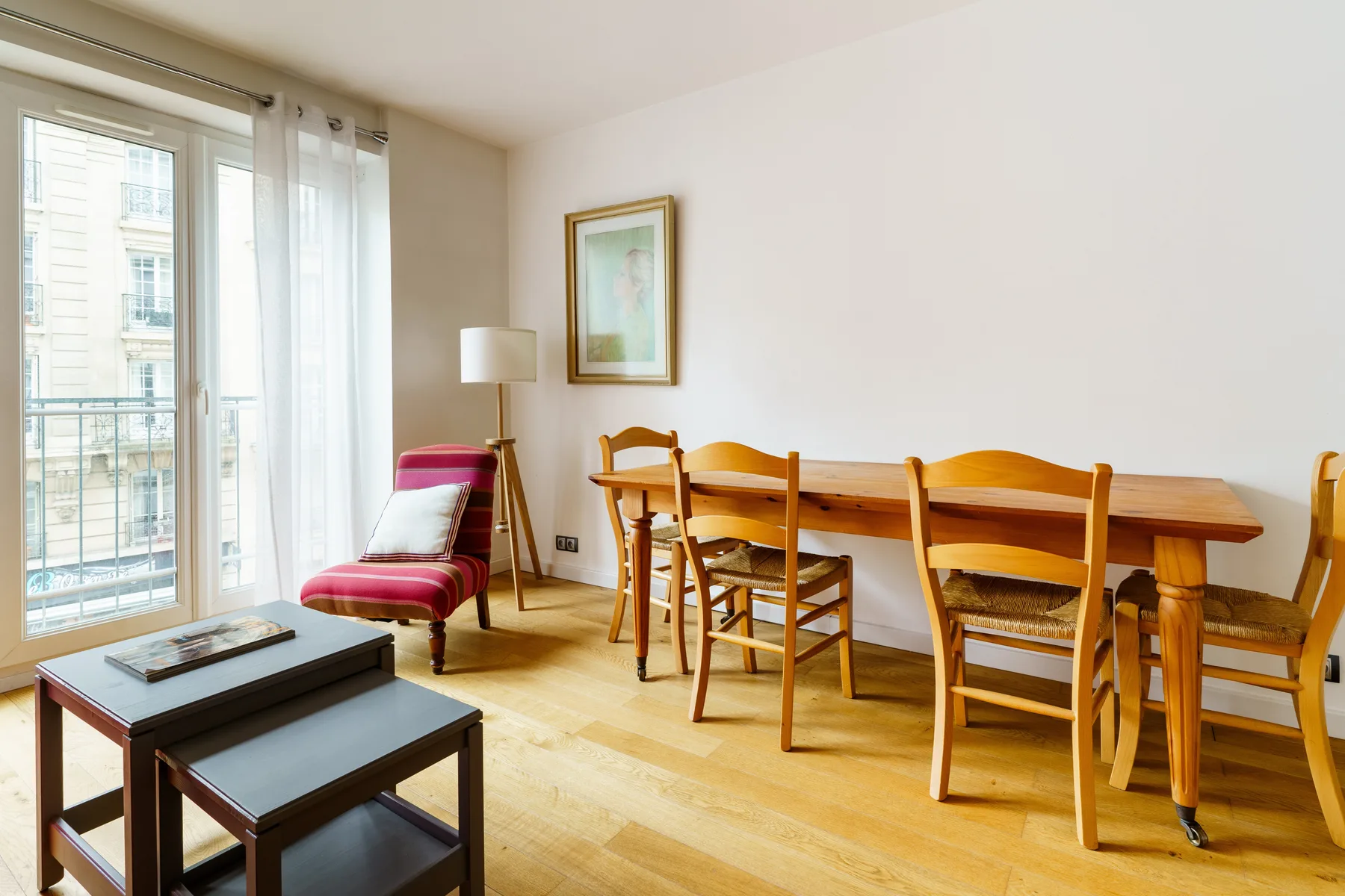 A dining area with a wooden table and chairs beside tall windows.