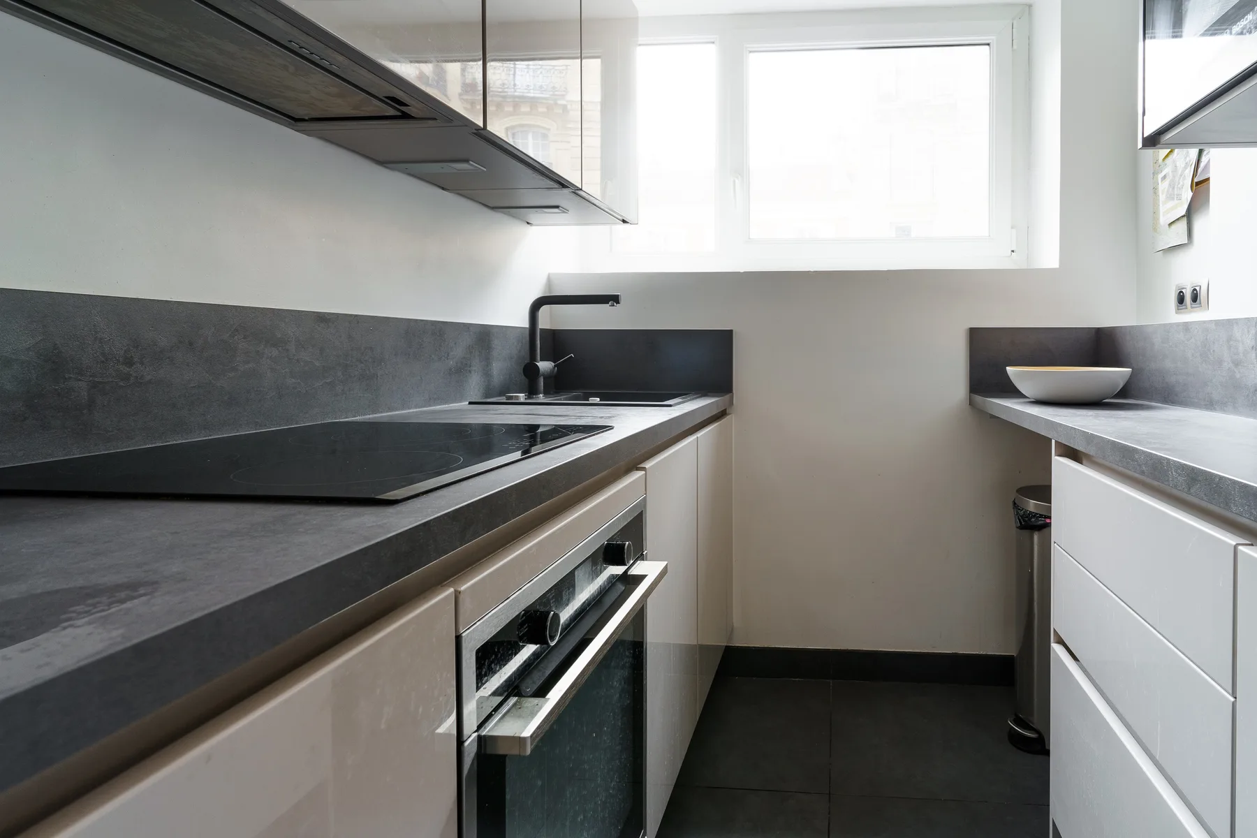 A modern kitchen with dark countertops and a large window.