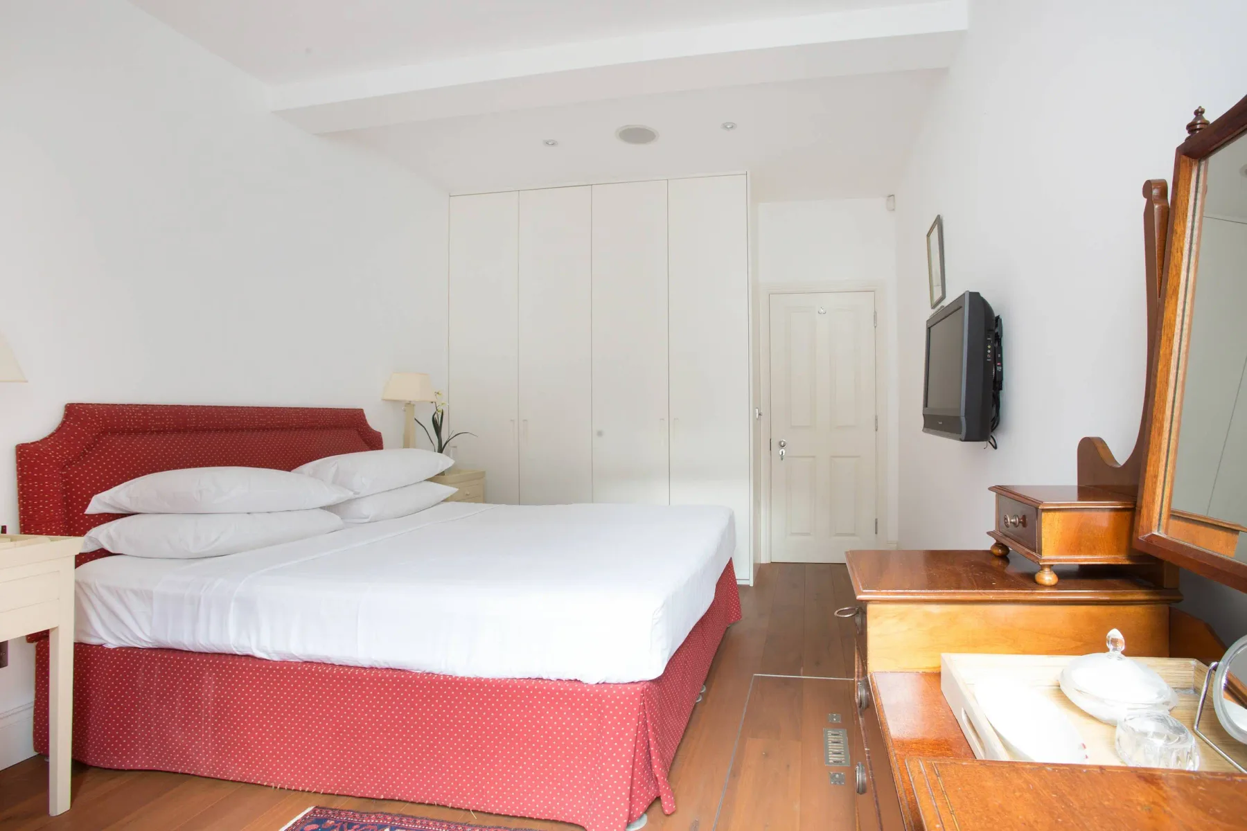 Un dormitorio con una cama bien hecha y un televisor montado en la pared.