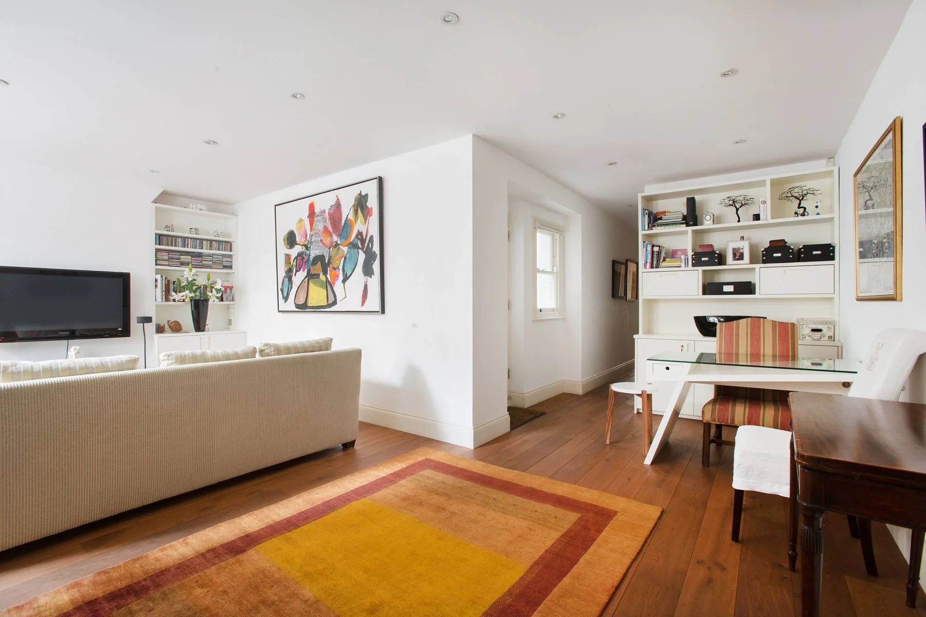 Luminoso salón-comedor con sofá, mesa y estanterías empotradas.
