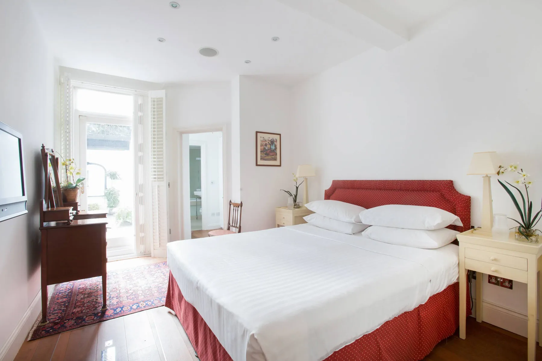 Un dormitorio luminoso con una cama grande, cabecero rojo y mesillas.