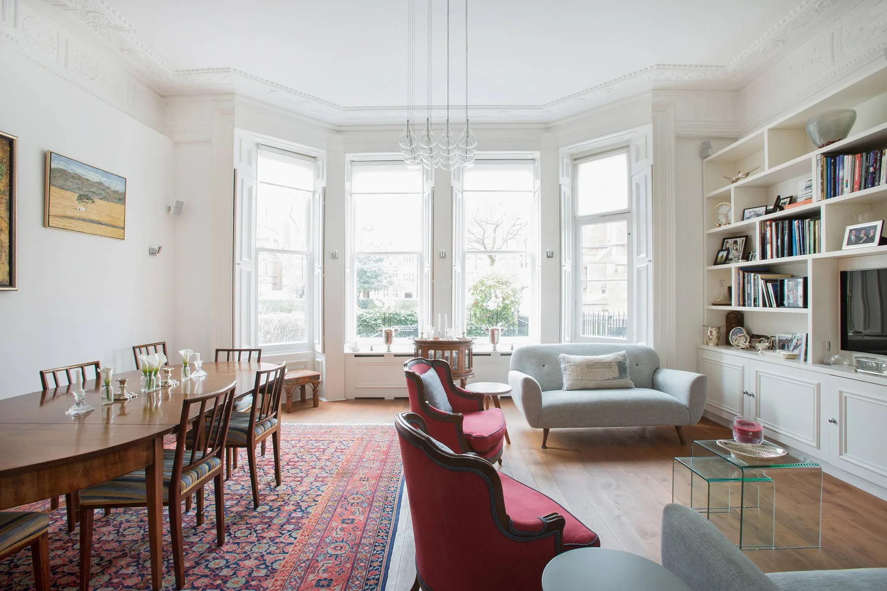 Una luminosa sala de estar y comedor con grandes ventanas y una estantería empotrada.