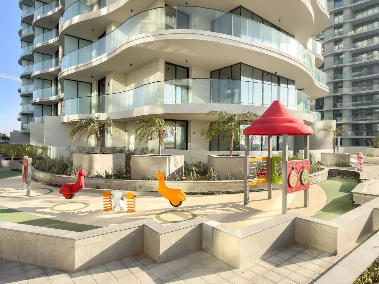 Una zona de juegos infantiles con equipos coloridos está junto a un edificio moderno.