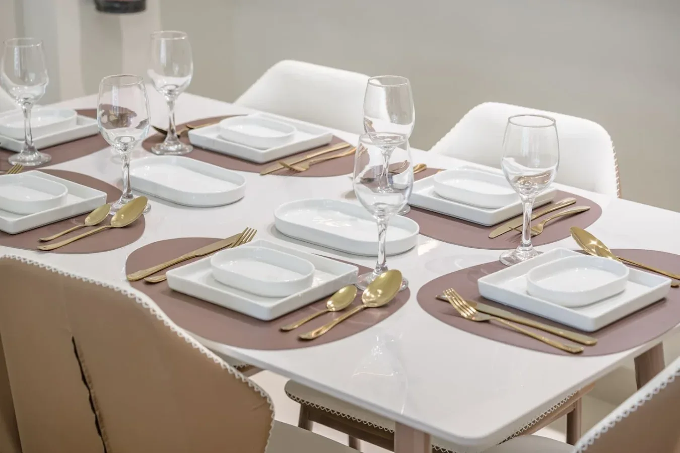 Una mesa de comedor está puesta con platos blancos, manteles individuales y cristalería.