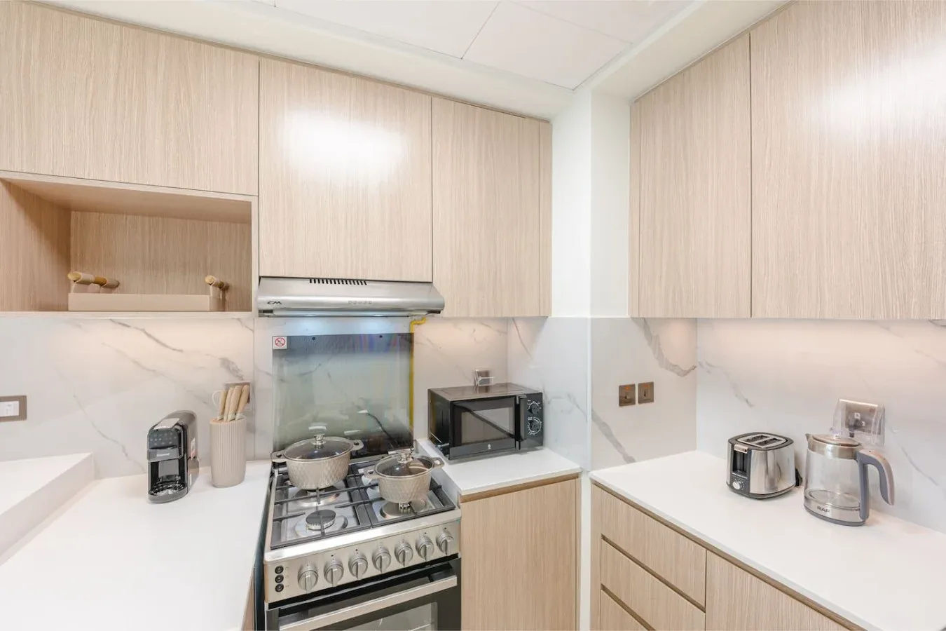 Una cocina luminosa con gabinetes de madera clara, encimeras blancas y una estufa de gas.