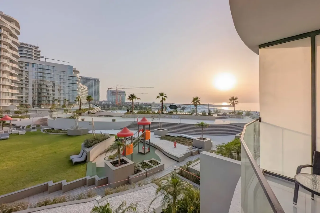 Un complejo residencial frente al agua domina jardines y un parque infantil al atardecer.