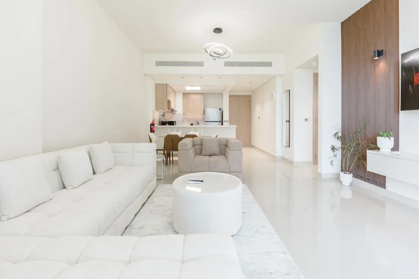 Una sala luminosa con asientos blancos, una mesa de centro redonda y una cocina abierta.