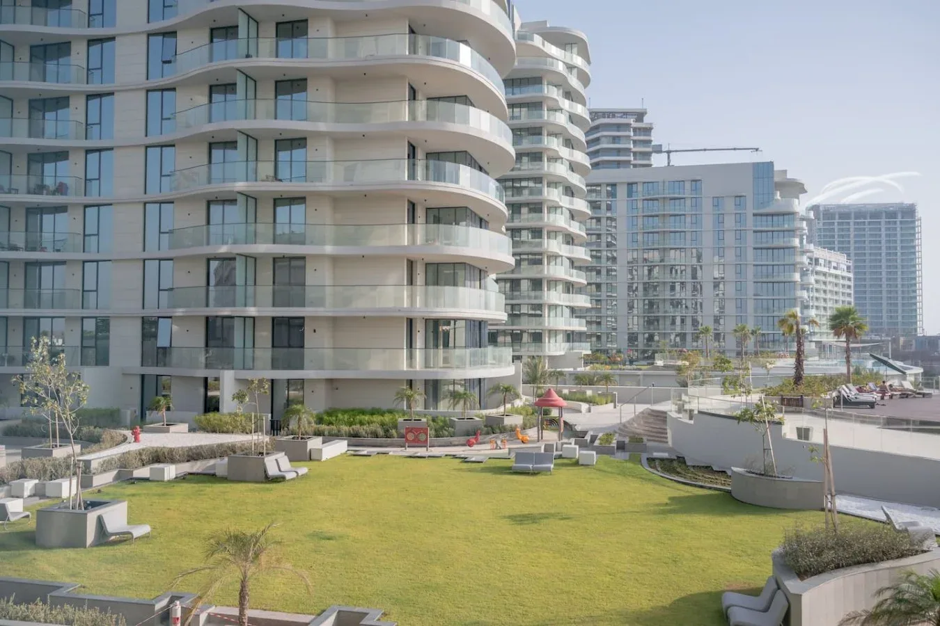 Edificios modernos de líneas curvas dan a un césped ajardinado con asientos al aire libre.