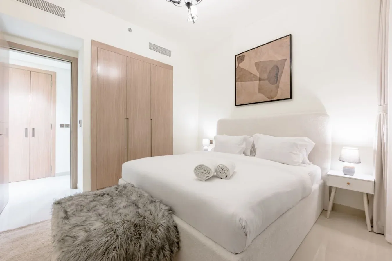 Un dormitorio luminoso con una cama tendida y una obra enmarcada sobre el cabecero.