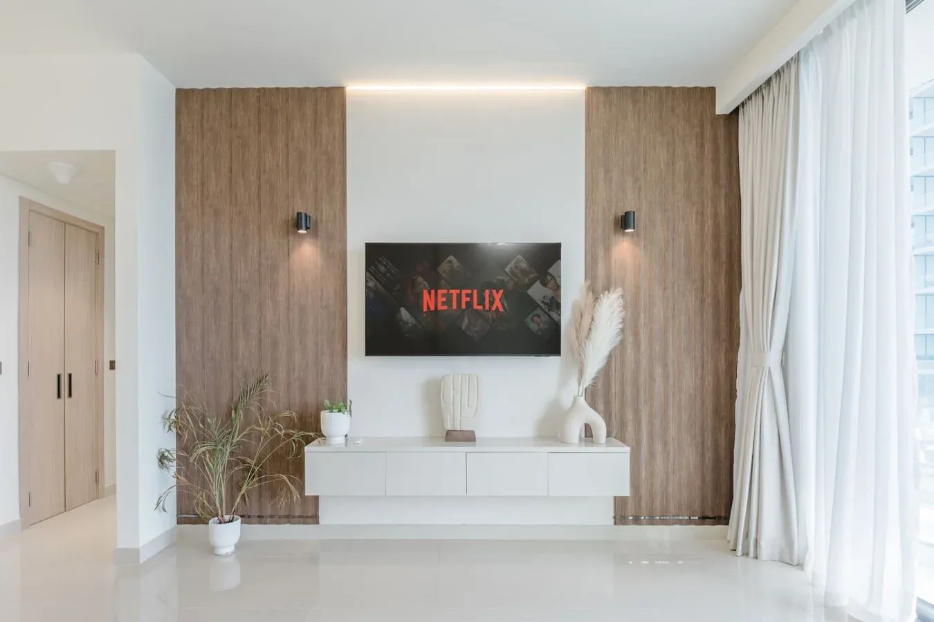 Una sala luminosa tiene un televisor montado en la pared sobre una consola blanca.