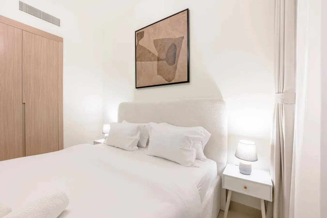 Un dormitorio luminoso con una cama bien hecha y un cuadro sobre el cabecero.
