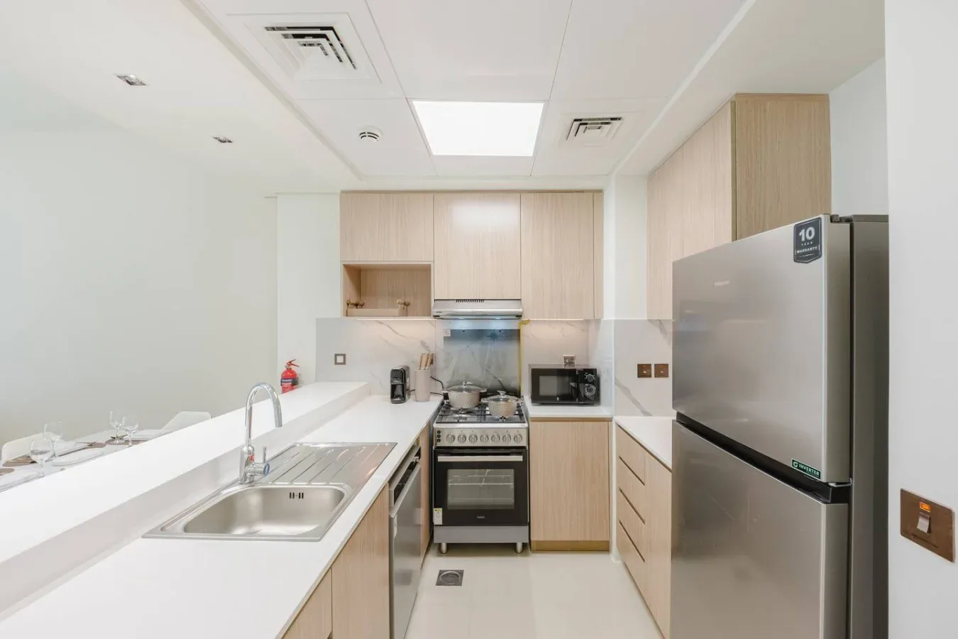 Una cocina compacta con gabinetes de madera clara, fregadero y electrodomésticos de acero inoxidable.