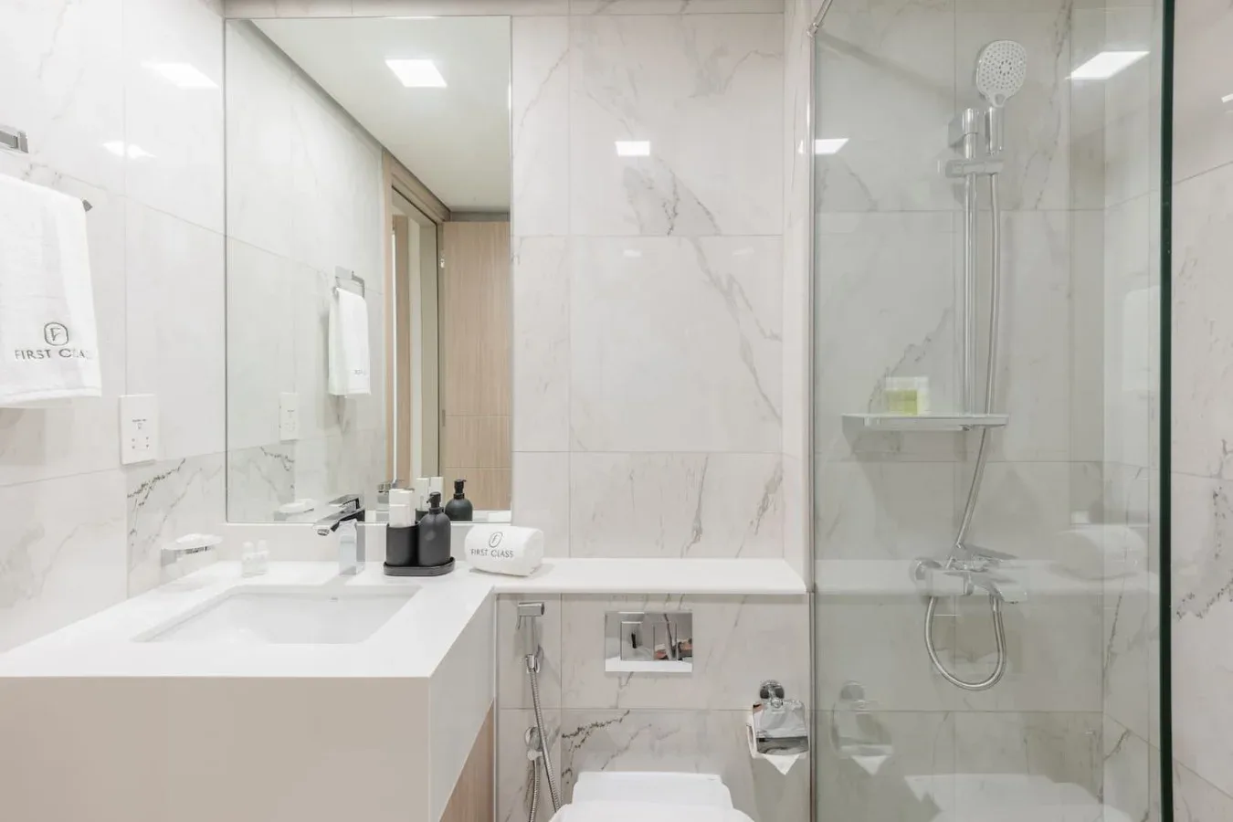 Un baño luminoso con azulejos, lavabo, inodoro y ducha de vidrio.
