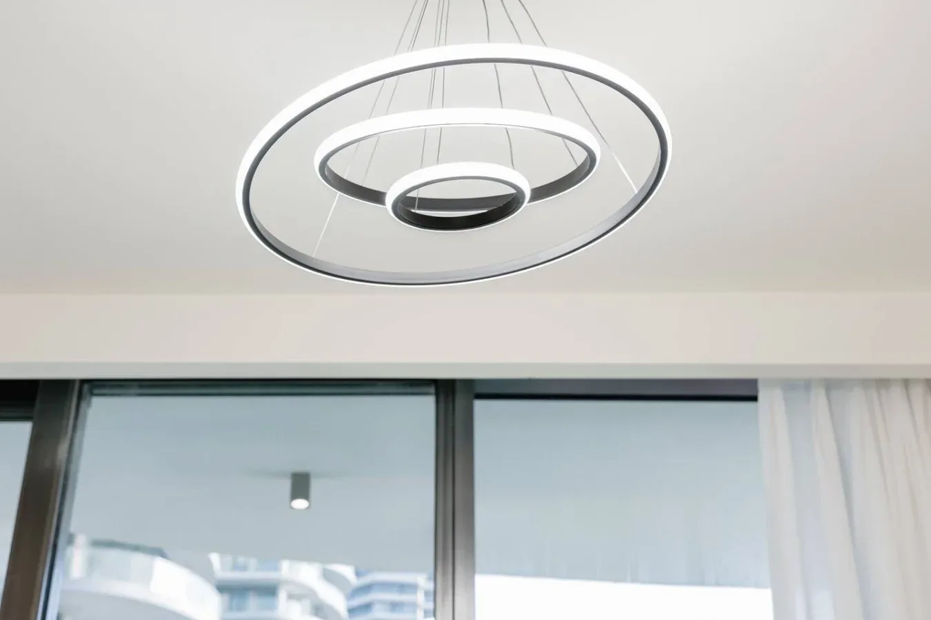 Un interior moderno muestra una lámpara colgante circular sobre grandes ventanas.