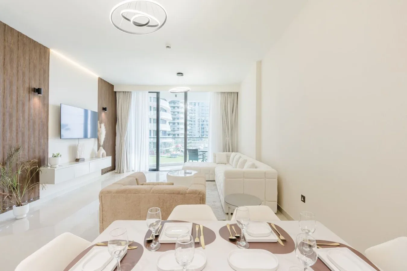 Una luminosa zona de estar y comedor tiene asientos, un televisor y ventanales.