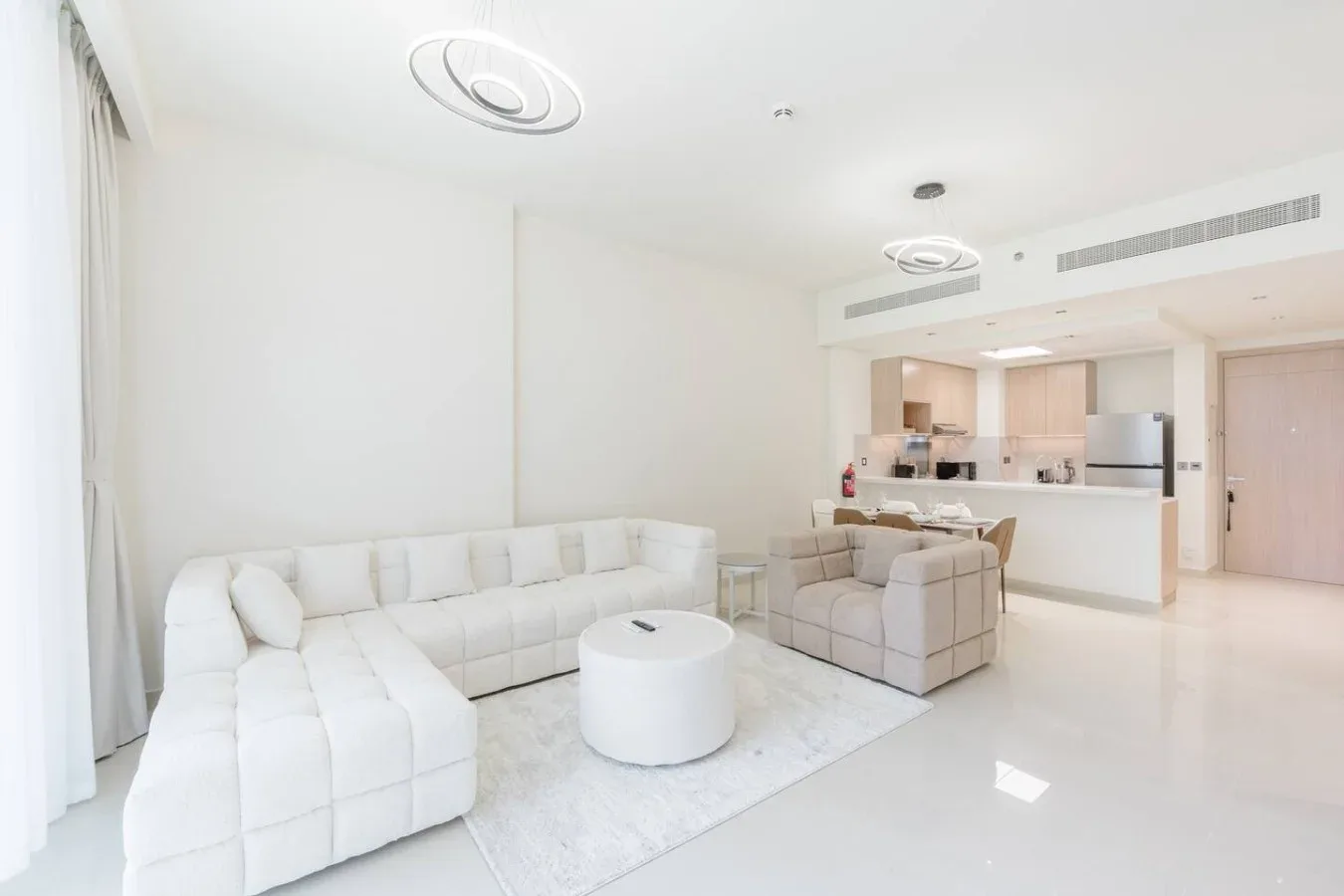 Una sala luminosa con asientos blancos, una mesa de centro redonda y una cocina abierta.
