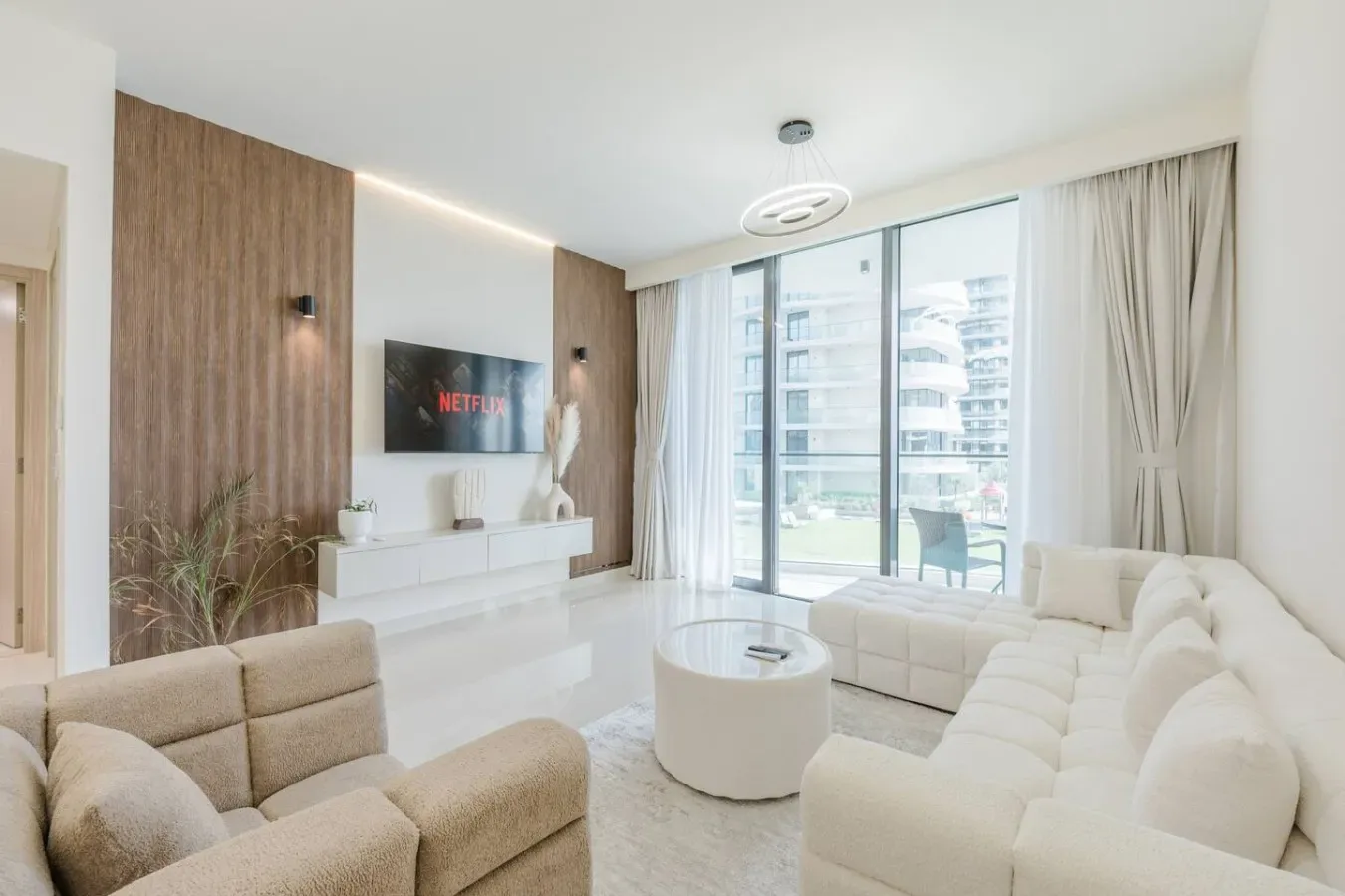 Una sala luminosa con asientos claros, un televisor y grandes ventanales.