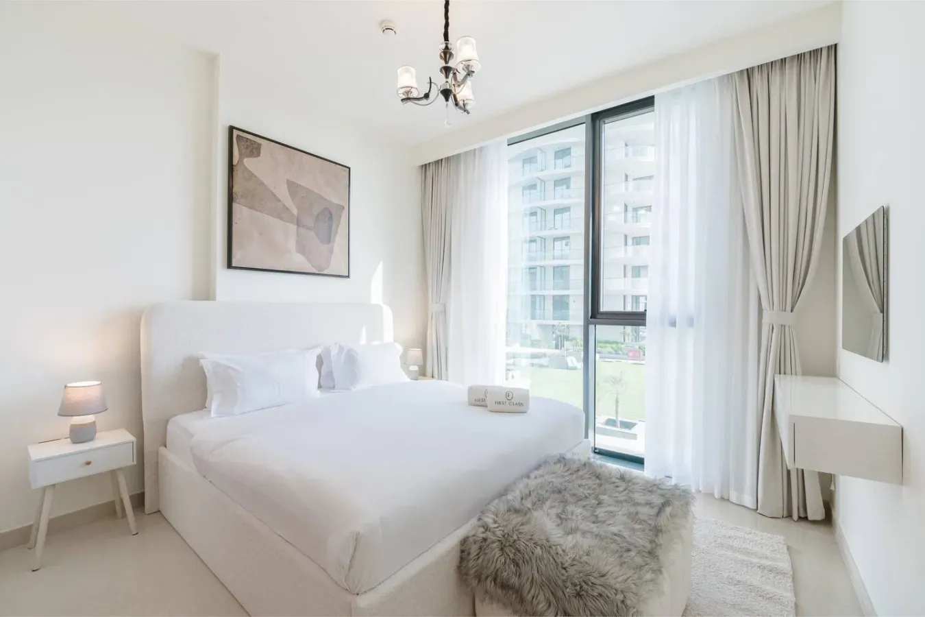 Un dormitorio luminoso con una cama blanca junto a grandes ventanales y cortinas.