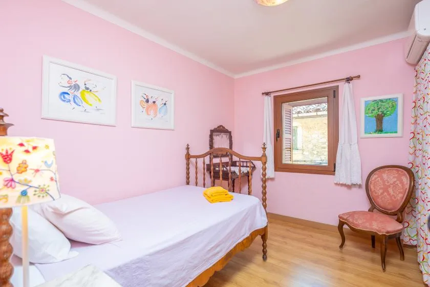 Un dormitorio rosa con una cama, una ventana y una silla de madera.