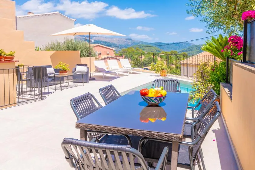 Una terraza soleada con comedor al aire libre ofrece vistas a una piscina y colinas.