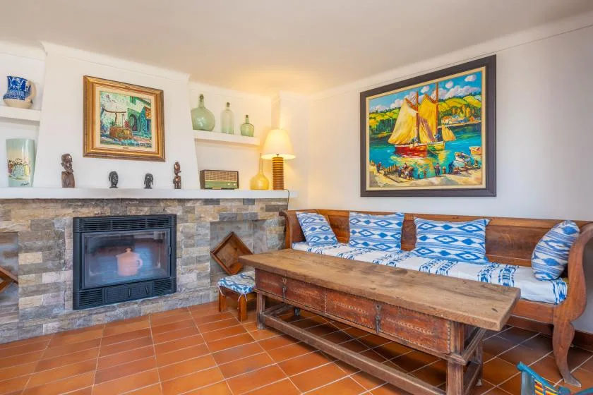 Una sala de estar con chimenea revestida de azulejos y asientos estampados alrededor de una mesa de centro de madera.