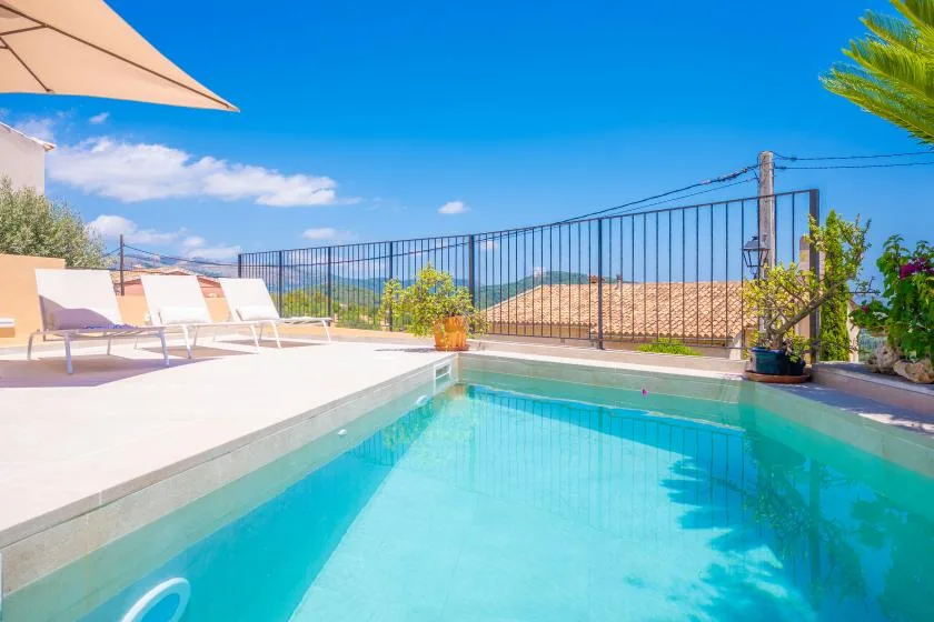 Una piscina al aire libre junto a un patio soleado con asientos reclinables.