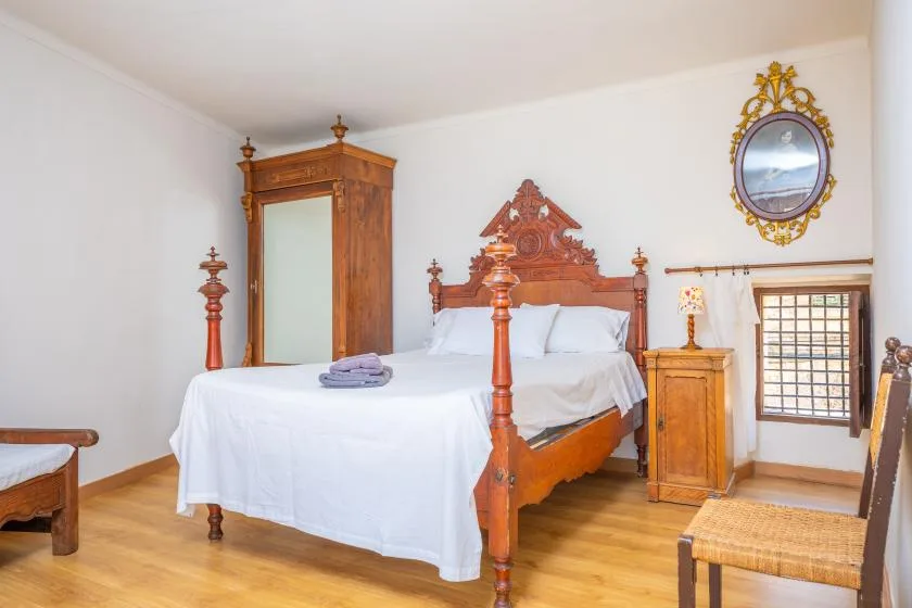 Un dormitorio con una cama de madera tallada, ropa de cama blanca y un armario alto.
