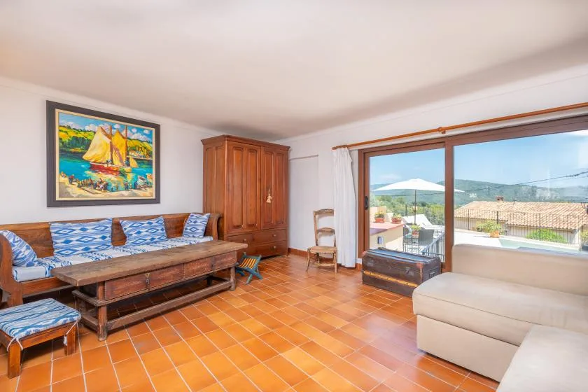 Una sala de estar con asientos, una mesa de madera y una ventana grande con vistas a las colinas.