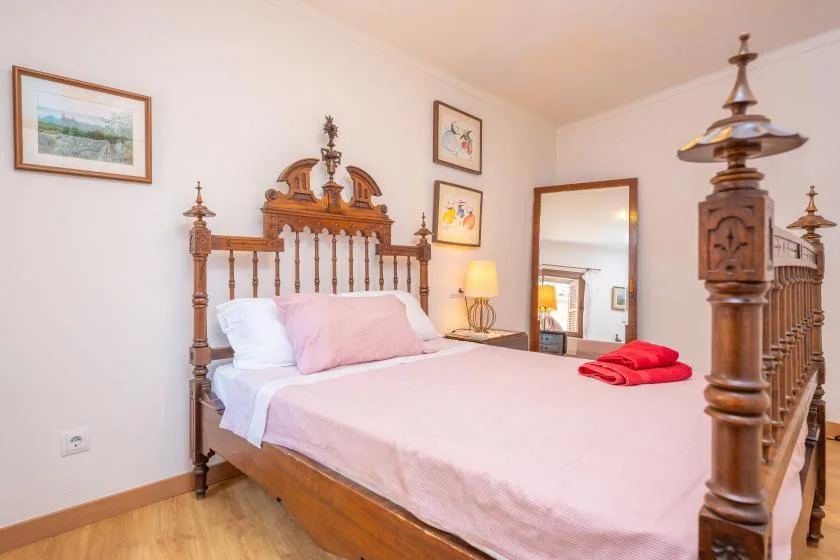 Un dormitorio con una cama de madera tallada, ropa de cama clara y cuadros enmarcados.