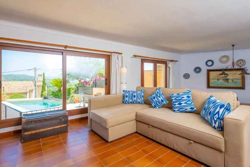 Una sala de estar con un sofá seccional beige y grandes ventanas con vista al patio.