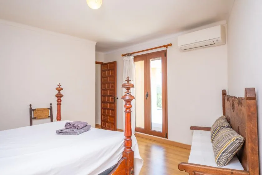 Un dormitorio con una cama de madera, un banco y una puerta con paneles de vidrio.