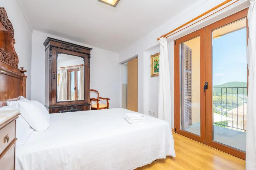 Un dormitorio luminoso con una cama blanca y puertas de cristal hacia un balcón.