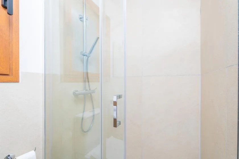 Un baño alicatado con una ducha de vidrio y accesorios de ducha en la pared.